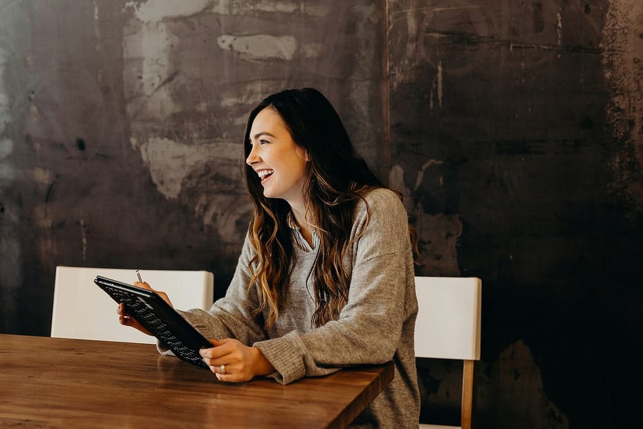 A woman sits at a table holding a tablet, getting ready to file her HMRC self assessment.