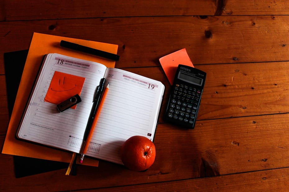 Black calculator, orange, and notebook on a table—essentials for completing the SA100 form.