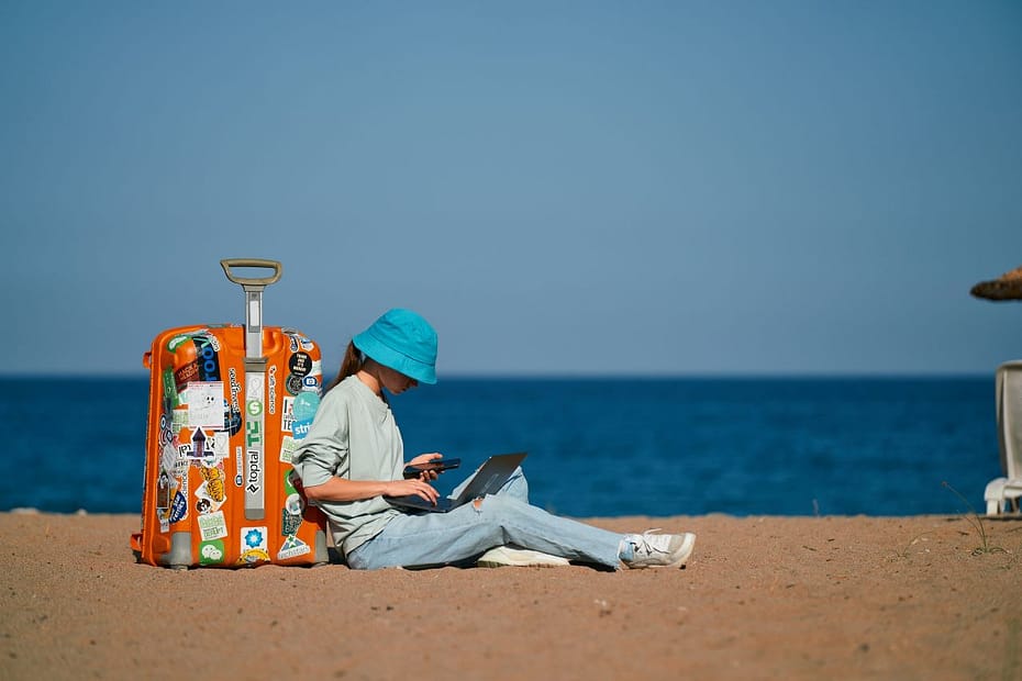Remote worker sits on a beach with a suitcase, representing the remittance basis for expats abroad.